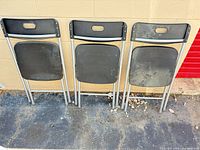 Rear view of three folding chairs showing black plastic panels and gray metal frames