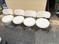 Four matching white bouclé dining chairs with gold frames side by side on driveway