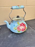 Front view of floral enamel teapot with glass lid and handle upright