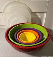 Stacked rainbow-colored ceramic bowls nested together with white plastic lids behind