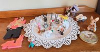 Full lot overview on shelf showing all bunny figurines, wooden puzzles, trinket tin, knitted bunny, birdhouse, cart, doily