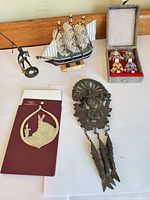 Group shot showing all five items: pewter ornament, metal mobile, mask box, model ship, fisherman figurine