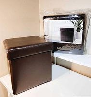 Assembled brown faux leather ottoman beside packaged identical ottoman