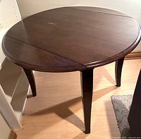 Full view of round dark brown dining table with drop leaves extended
