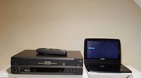 Front view of Toshiba VCR, Philips portable DVD player powered on, remote on top