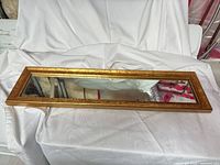 Full view of rectangular gilded gold framed mirror on white drape