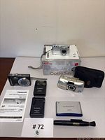 All cameras, chargers, case, manual, cleaning pen and packaging laid out on table