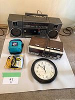 Overall lot showing boombox, clock radio, Walkman with earphones, wall clock, blue pouch