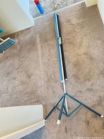 Projection screen collapsed on tripod base, showing full stand and housing