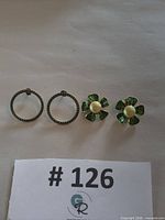 Both earring pairs arranged on surface: green stone pavé hoops and green enamel flower clip-ons with faux pearl centers
