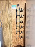 Full view of vertical black metal wine rack mounted on wood panel wall