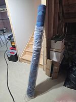 Rug rolled and wrapped in plastic leaning against stairs