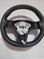 Front view of black leather Tesla steering wheel without airbag, wiring harness visible