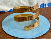 Side view of hammered gold-tone spiral bangle showing three coils and finish