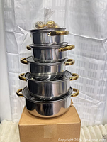stacked view of five stainless steel pots with gold-tone handles and lid knobs bagged on top