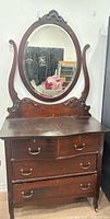 Front view showing dresser, four drawers, oval mirror, carved supports, brass pulls