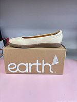 Side view of left Earth Landen ivory flat on branded box