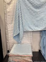 packaged stack of blue towels with one unfolded hanging and another pack beneath