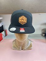 Front view of black flat bill hat showing leather Frontier Walleye Slayer patch and Richardson sticker