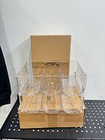 Front view showing assembled clear acrylic rack with four tiers on cardboard boxes