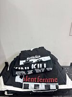 Stack of boxed/folded black graphic T-shirts showing Violent Femme and other prints