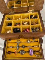 Open jewelry box showing divided top compartment with assorted earrings and lower ring rolls with eight rings