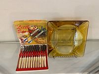 Amber glass ashtray beside boxed spoons, full lot overview