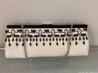 Front view of white clutch purse with black bead fringe and silver chain
