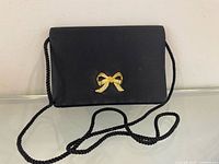 Front view of black satin clutch showing gold-tone bow ornament and rope strap