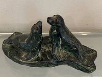 Full view of mottled green stone sculpture with two seals on rocky base