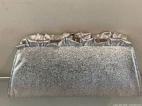 Front view of silver metallic clutch showing ruffled trim and clasp