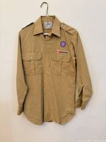 Full front view of khaki Scouts Canada uniform shirt on hanger