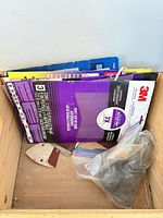 Packaged 3M sandpaper sheets and loose sheets inside wooden crate