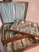 Oak chest open showing three trays loaded with flatware including knives with celluloid handles