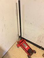 Full view of red MotoMaster floor jack with handle upright