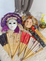 two porcelain carnival masks and eight fans displayed