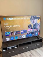Front view of Sony KD-85X85J powered on displaying Google TV home screen, shows slim bezel and twin feet
