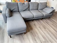 Full view of assembled L-shape sofa showing four seats, chaise module, both bolster pillows and legs