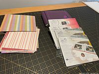 Stack of patterned cardstock sheets, purple 6x6 album and packaged Creative Memories 5x7 refill packs on cutting mat