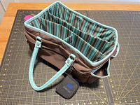 Overall view of tote, open top, brown exterior, aqua handles, striped interior compartments