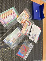 Overall lot showing several sealed packs of border/sticker strips and blue storage wallet on cutting mat