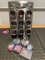 Front view of stainless steel rack with magnetic tins and plastic cases of embellishments in foreground