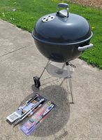 Full view of Weber grill with utensils in packages on ground