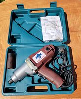Impact wrench with cord seated in open teal case with socket and manual visible