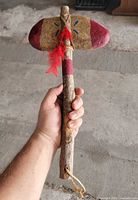 Full view of tomahawk in hand showing size, paint, and feather detail