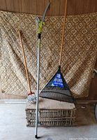 All three garden tools leaned upright: leaf rake, rotary cultivator, pole pruner