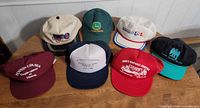 All seven vintage advertising caps displayed on table