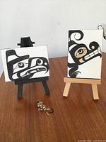 Both miniature canvases on easels with feather hook in foreground