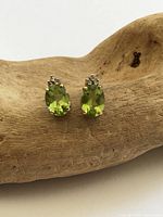 Front view of peridot and diamond stud earrings on wood prop