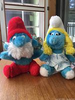 Papa Smurf and Smurfette plush toys side by side on table